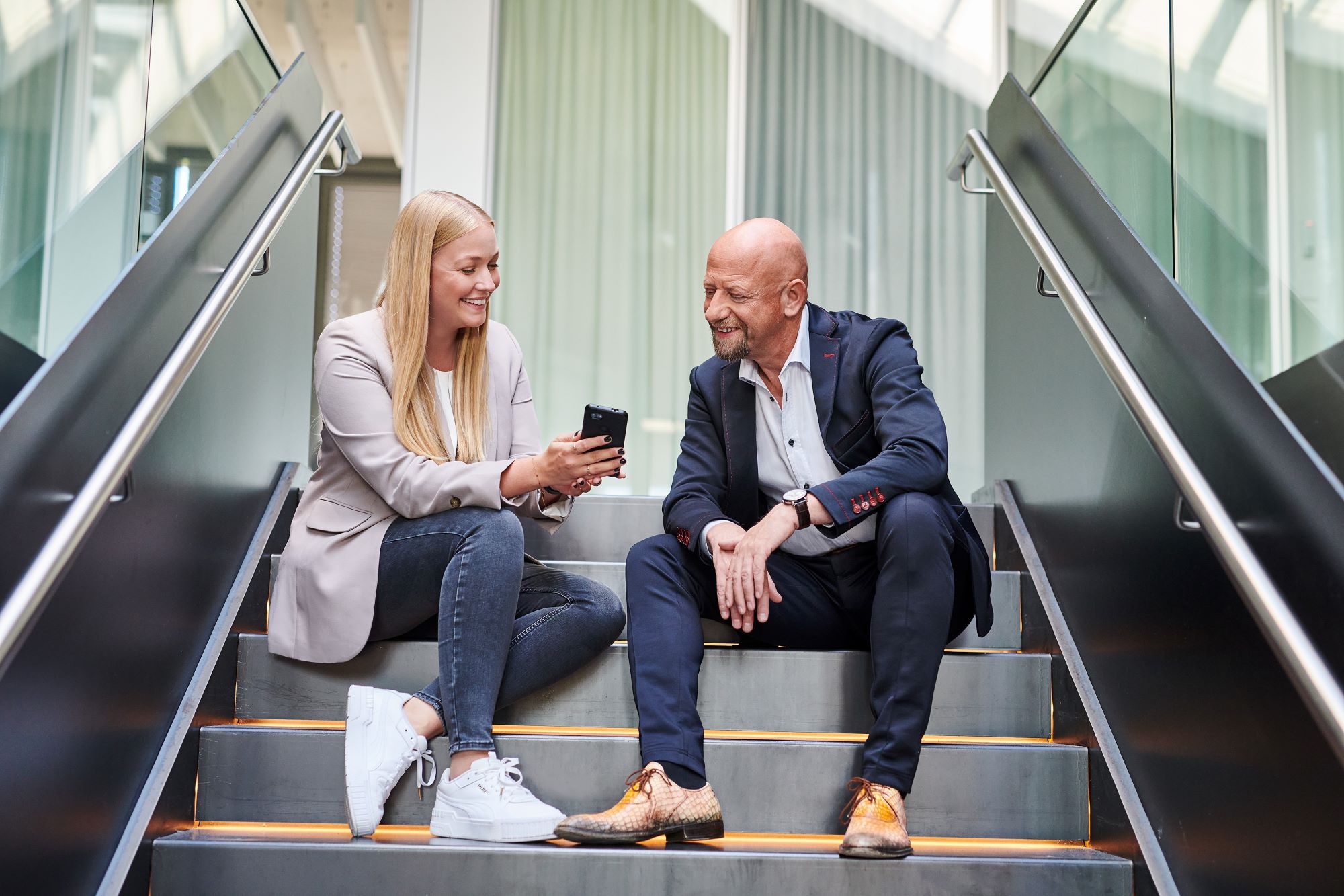 Mitarbeiterin zeigt einem Kollegen über ihr Handy eine Stelle für Berufseinsteiger:innen.