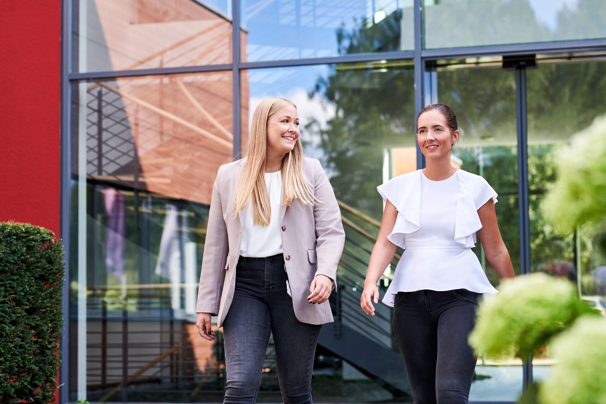 Zwei Mitarbeiterinnen laufen lächend über den Campus und sind glücklich ihren Traumjob gefunden zu haben.