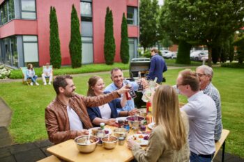 Mitarbeitenden sitzen zusammen beim Grillen und stoßen gemeinsam an.