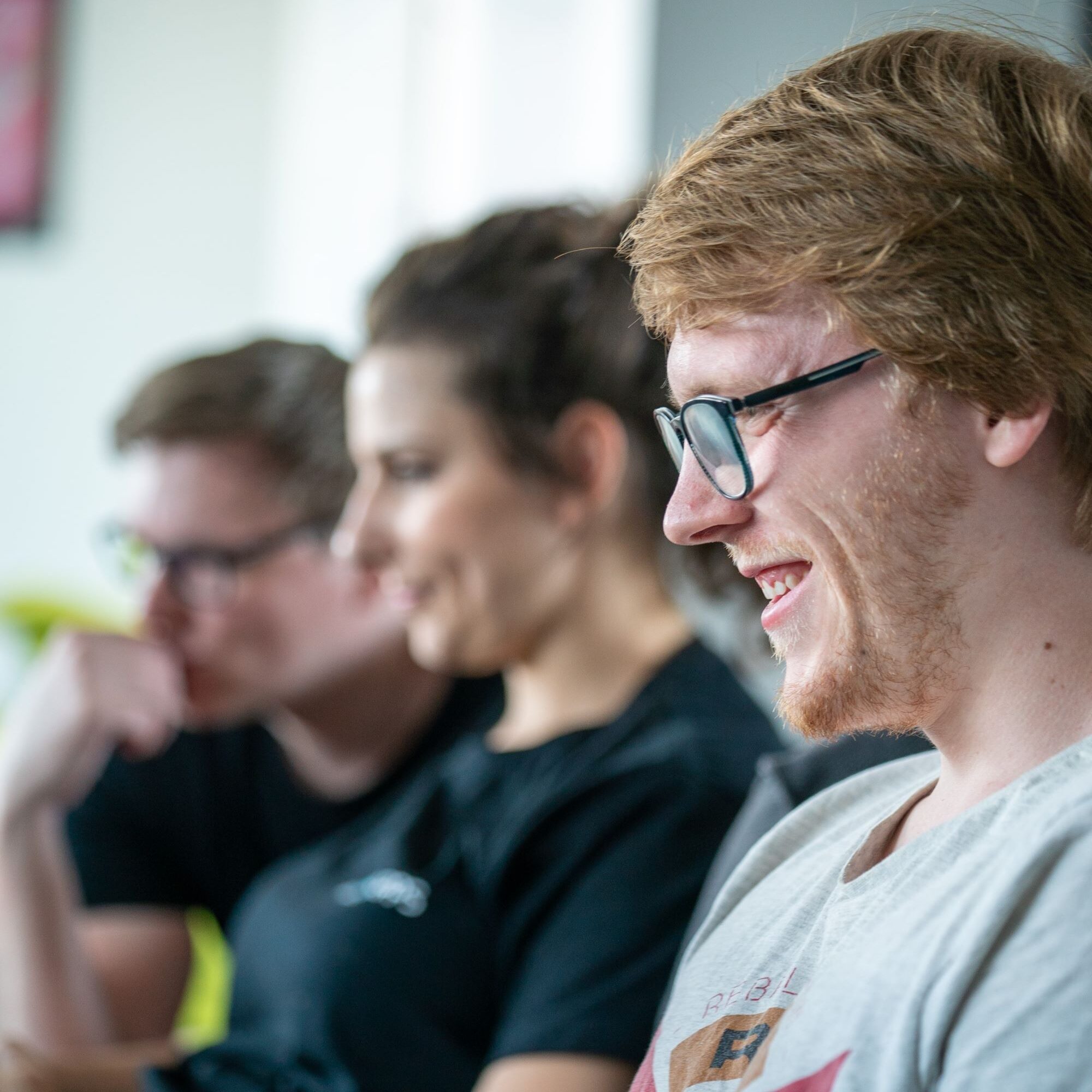 Mitarbeitenden sitzen nebeneinander und arbeiten und lachen zusammen.