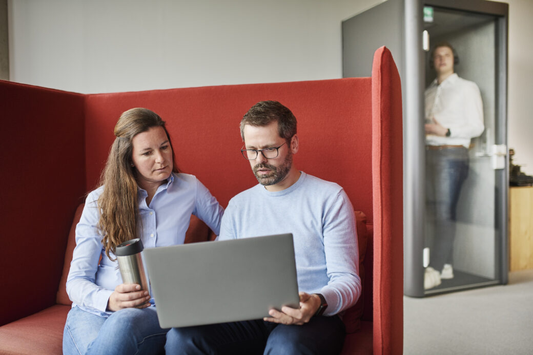 Zwei erfahrene Kollegen:innen unterhalten sich angeregt vor dem Laptop.